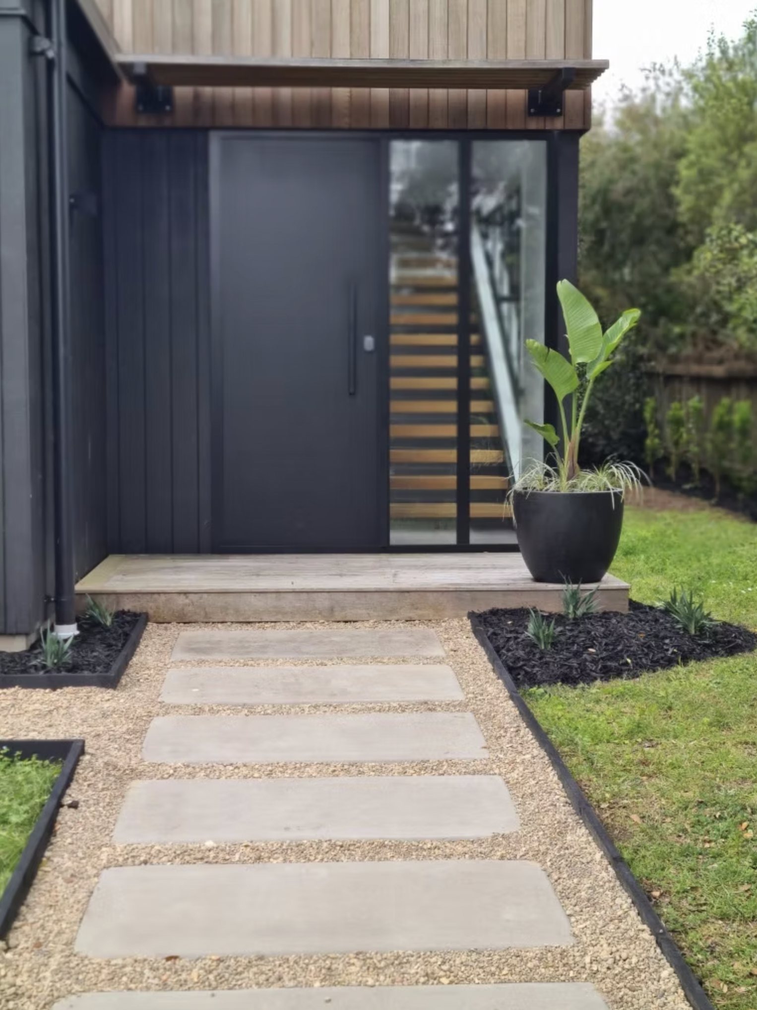 Dark architectural home entrance with a stone stepping path and specimen palm